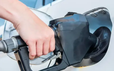 Dłoń trzyma pistolet paliwowy, rozpoczynając tankowanie samochodu.