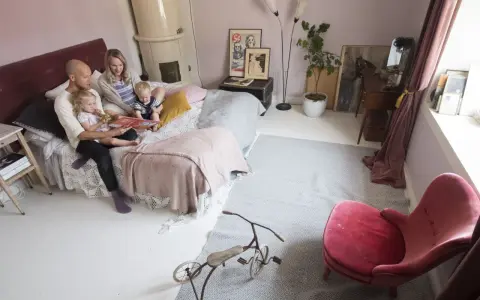 Familjen myser i sängen, pappan läser en bok för barnen. Ett litet bo med barn som njuter av stunden.
