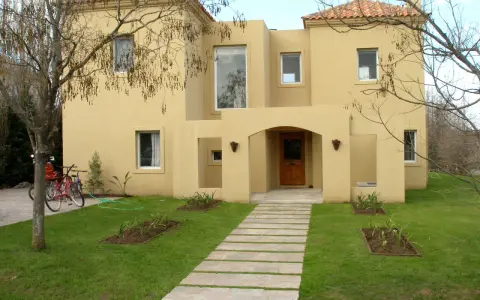 Una encantadora casa color arena con techo de tejas rojas, un camino de losas y dos bicicletas aparcadas en el jardín.