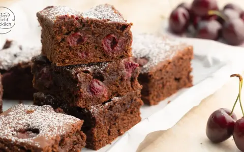 Saftige Stücke von Omas Schoko-Kirsch-Kuchen, bestäubt mit Puderzucker. Kirschen sind im dunklen Teig sichtbar.