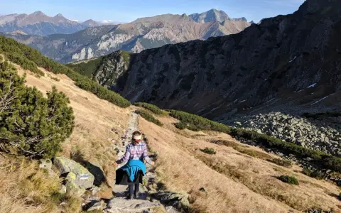 Osoba wędruje kamienistym szlakiem w Tatrach. Widok na góry i dolinę, idealne tatry szlaki dla średnio zaawansowanych.