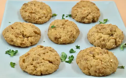 Sei polpette di patate dorate e croccanti, guarnite con prezzemolo fresco, su un piatto azzurro.