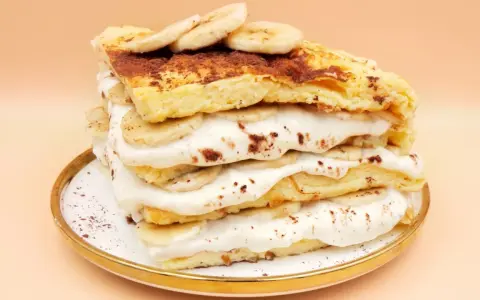 Wysoki omlet z bananem, przełożony kremem i plasterkami banana, posypany kakao. Pyszny deser na talerzyku.