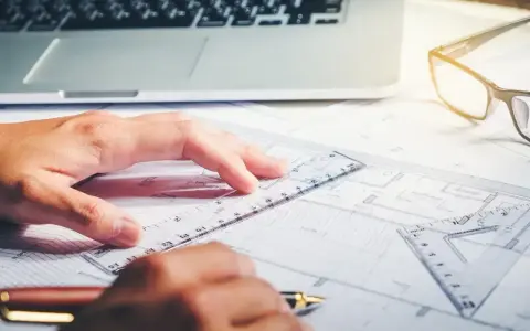 Rysowanie planów, laptop i okulary na biurku. Zastanawiasz się, ile zarabia architekt?