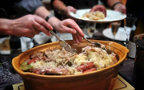 Un plat généreux de choucroute garnie, spécialité de la gastronomie alsacienne, est servi. Des mains servent ce délice, promesse d'une savoureuse nourriture d'Alsace.
