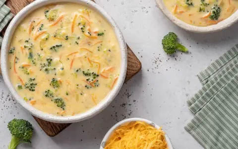 Un cremoso puré de brócoli y zanahoria, con trozos visibles de brócoli y ralladura de queso, servido en un cuenco blanco.
