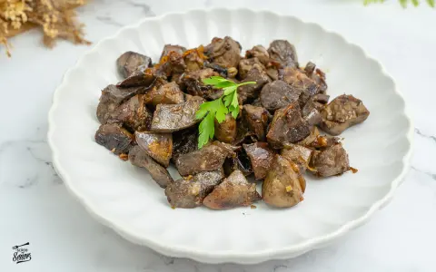 Plato de asadura de cordero salteada con ajo y perejil, servido en un plato blanco con borde ondulado.