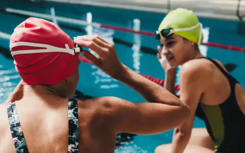 Deux nageuses se préparent pour une course de nage brasse. L'une ajuste ses lunettes, l'autre sourit.