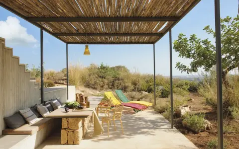 Porches sencillos y bonitos con mesa de piedra, asientos cómodos y tumbonas bajo un techo de madera.