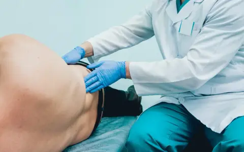 Lekarz w białym fartuchu i niebieskich rękawiczkach bada pacjenta. To badanie, które wykonuje lekarz, kto bada prostatę.