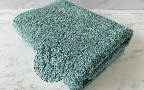 A folded teal terry cloth towel with a magnified inset showing its plush texture.