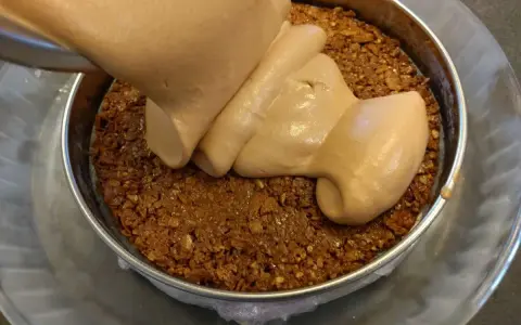 Une crème onctueuse est versée sur une base de croustillant praliné feuilletine dans un cercle à pâtisserie.