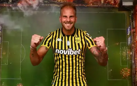 Uros Racic, con su nueva camiseta a rayas amarillas y negras, celebra con los puños en alto. El fondo simula un campo de fútbol con bengalas.