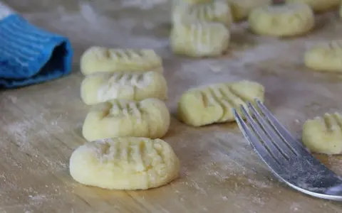 Frisch geformte italienische Gnocchi liegen auf bemehltem Holz. Eine Gabel und ein blauer Lappen sind ebenfalls zu sehen.