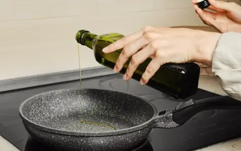 Ręka wylewa oliwę z oliwek do smażenia na patelnię.