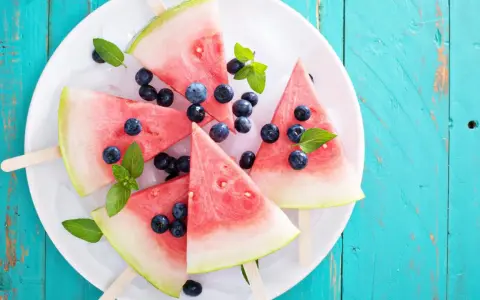Erfrischendes Wassermelonen Eis mit Blaubeeren und Minze auf Eiswürfeln, serviert auf einem weißen Teller.