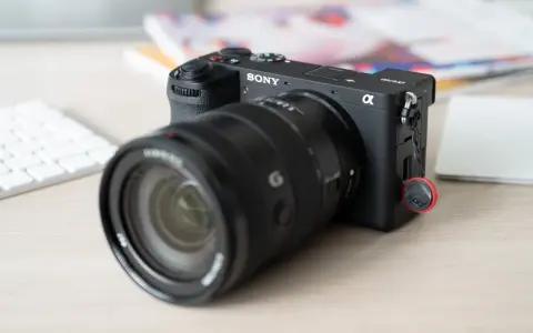 Appareil photo Sony Alpha a6700 prêt pour un test. Un objectif noir est monté, avec un clavier blanc et des documents flous en arrière-plan.