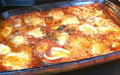 Parmigiana di melanzane appena sfornata, dorata e filante, in una teglia di vetro.