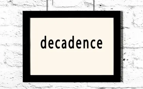 Czarny prostokątny obraz z napisem "decadence" na jasnym tle, wiszący na białej ceglanej ścianie. Symbol dekadentyzmu.
