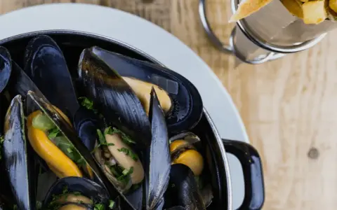 En stor kastrull med ångande blåmusslor, perfekt för en måltid med vin till moules frites. Pommes frites syns i bakgrunden.