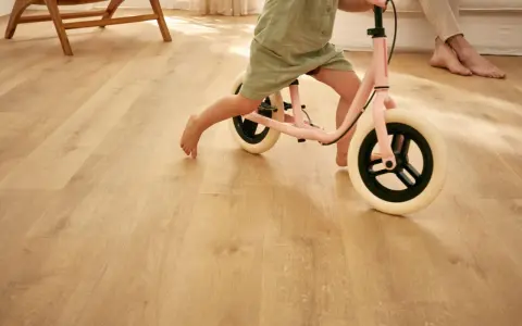 Un enfant apprend à faire du vélo d'équilibre sur un sol de salle de jeux en bois clair.
