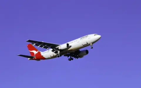 Samolot Qantas z charakterystycznym kangurem na ogonie, symbolizujący najbezpieczniejsze linie lotnicze, leci na tle błękitnego nieba.