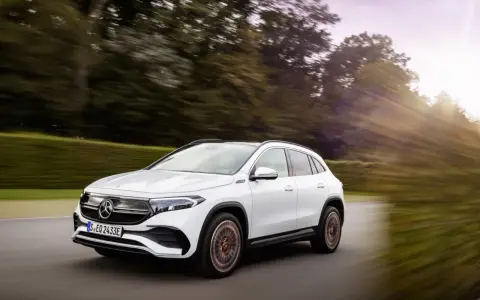 Un Mercedes EQA blanco circula por una carretera rodeada de árboles. Las **mercedes eqa medidas** son ideales para la ciudad y escapadas.