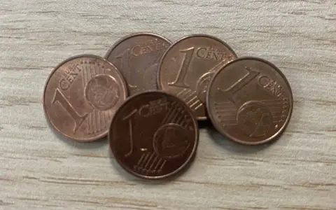 Cinq pièces de 1 centime d'euro, certaines semblant être une pièce de 1 euro rare valeur, sont disposées sur une surface en bois.