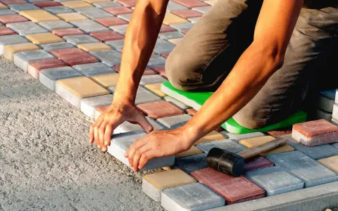 Ręce układają kolorową kostkę brukową na betonie. Powstaje równy wzór.