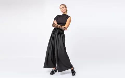 Elegancka kobieta w czarnych, szerokich spodniach i topie z siateczkowymi rękawami. Stylowe, lakierowane mokasyny to idealne buty do teatru.