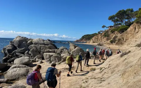 Une randonnée côtière ensoleillée, avec un groupe de randonneurs profitant d'une marche afghane le long d'une plage rocheuse et d'une falaise verdoyante.