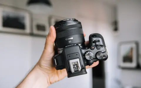 Dłoń trzyma aparat Canon z obiektywem 35mm, idealny dla amatora chcącego zacząć przygodę z fotografią.