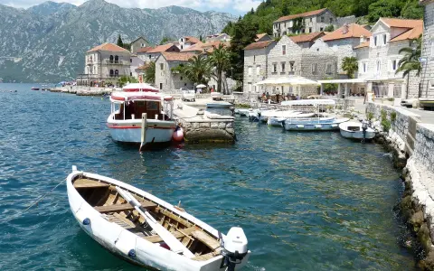 Port w Czarnogórze, łodzie na wodzie, góry w tle. Ceny rejsów mogą być różne, warto sprawdzić.