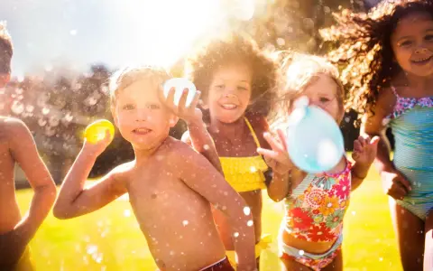 Niños riendo y jugando con globos de agua bajo el sol. Salpicaduras y diversión garantizada en estos juegos acuáticos.