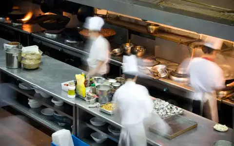 Chefs en movimiento en una cocina profesional, con ollas humeantes y ingredientes listos. El "mise en place" es clave para la eficiencia.