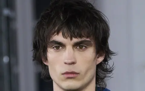 Joven con un corte de pelo mullet desordenado, mirada intensa y cejas marcadas.