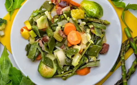 Menestra de verduras variadas con trozos de jamón en un plato blanco.