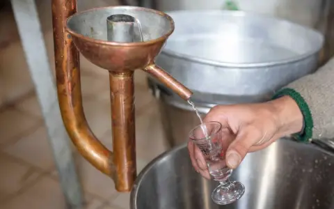 Ein Schnaps wird in ein Glas destilliert. Die Kupferapparatur zeigt, wie man Schnaps brennt.