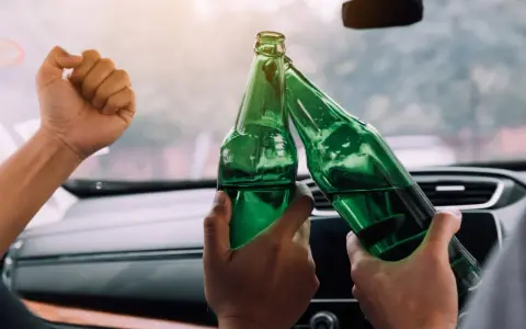 Dwie osoby w samochodzie wznoszą toast zielonymi butelkami piwa 0 5 procent.