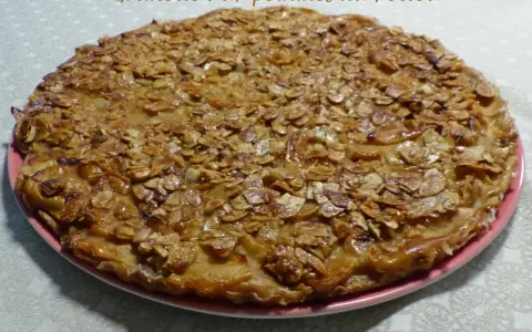 Gâteau rustique aux pommes et amandes effilées sur une assiette rose.