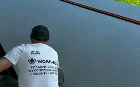 Pracownik w koszulce z napisem "POSADZKI ŻYWICZNE" kończy pracę nad nową, lśniącą posadzką.