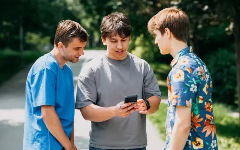 Trzech studentów dyskutuje, czy na studiach są wakacje. Jeden z nich pokazuje coś na telefonie.