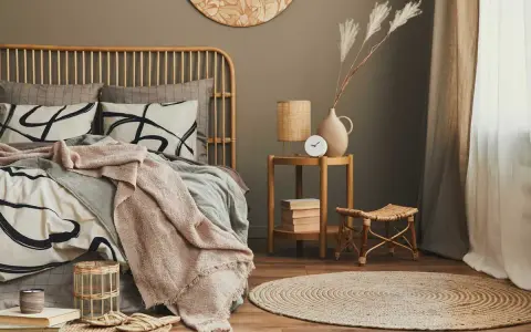 Dormitorio con cama de ratán, ropa de cama beige y gris, manta rosa, mesita auxiliar de madera y alfombra redonda.