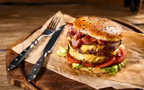 Podwójny burger z soczystym mięsem na burgery, serem, bekonem i warzywami, gotowy do zjedzenia z widelcem i nożem.