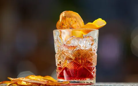 Klasyczny whisky old fashioned w kryształowej szklance, ozdobiony skórką pomarańczy i suszonym owocem.