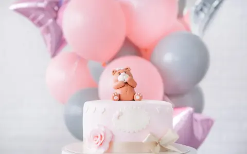 Uroczy topper na tort baby shower w kształcie misia siedzącego na różowym torcie, otoczony balonami w pastelowych kolorach.