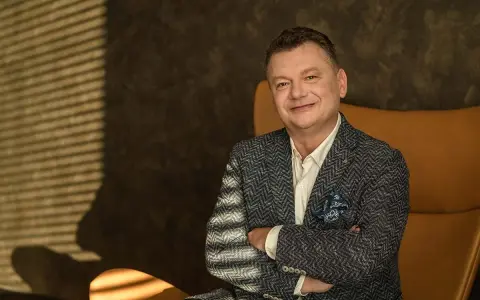 Uśmiechnięty mężczyzna, January Ciszewski, w eleganckiej marynarce siedzi w fotelu.