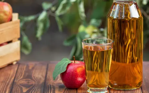 Manzana roja junto a un vaso y botella de vinagre de manzana para limpiar. Cosecha fresca en caja de madera al fondo.