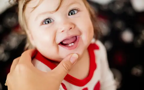 Ein lächelndes Baby mit blauen Augen zeigt stolz seine ersten Zähnchen. Das Baby zahnen ist ein aufregender Meilenstein!