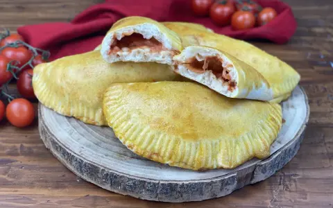 Panzerotti al forno dorati e ripieni di pomodoro e mozzarella filante, pronti per essere gustati.